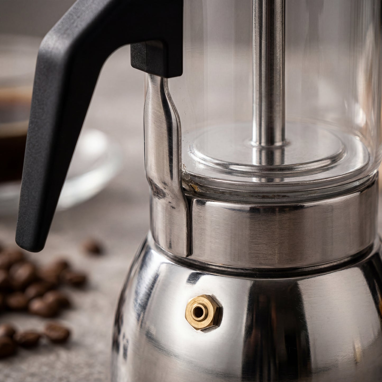 Gros plan de la valve en laiton sur la base en inox d'une cafetière italienne en verre.