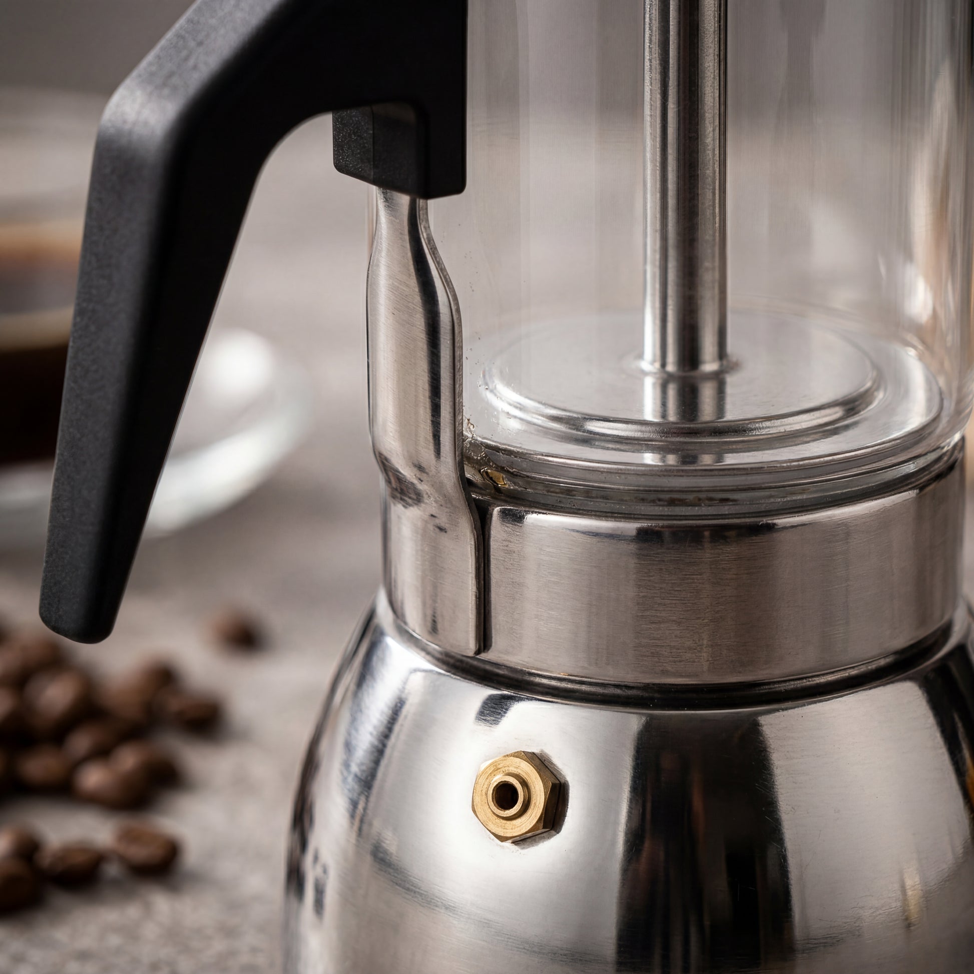 Gros plan de la valve en laiton sur la base en inox d'une cafetière italienne en verre.