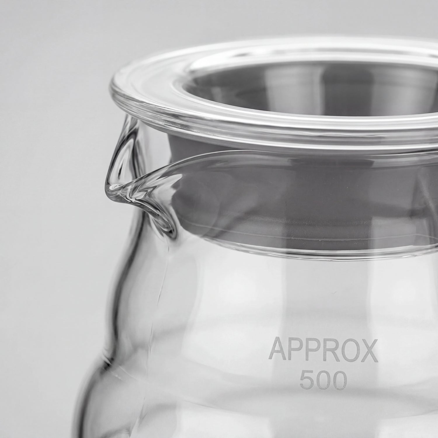 Gros plan du bec verseur et du couvercle en verre à liseré inox d'une carafe à café.