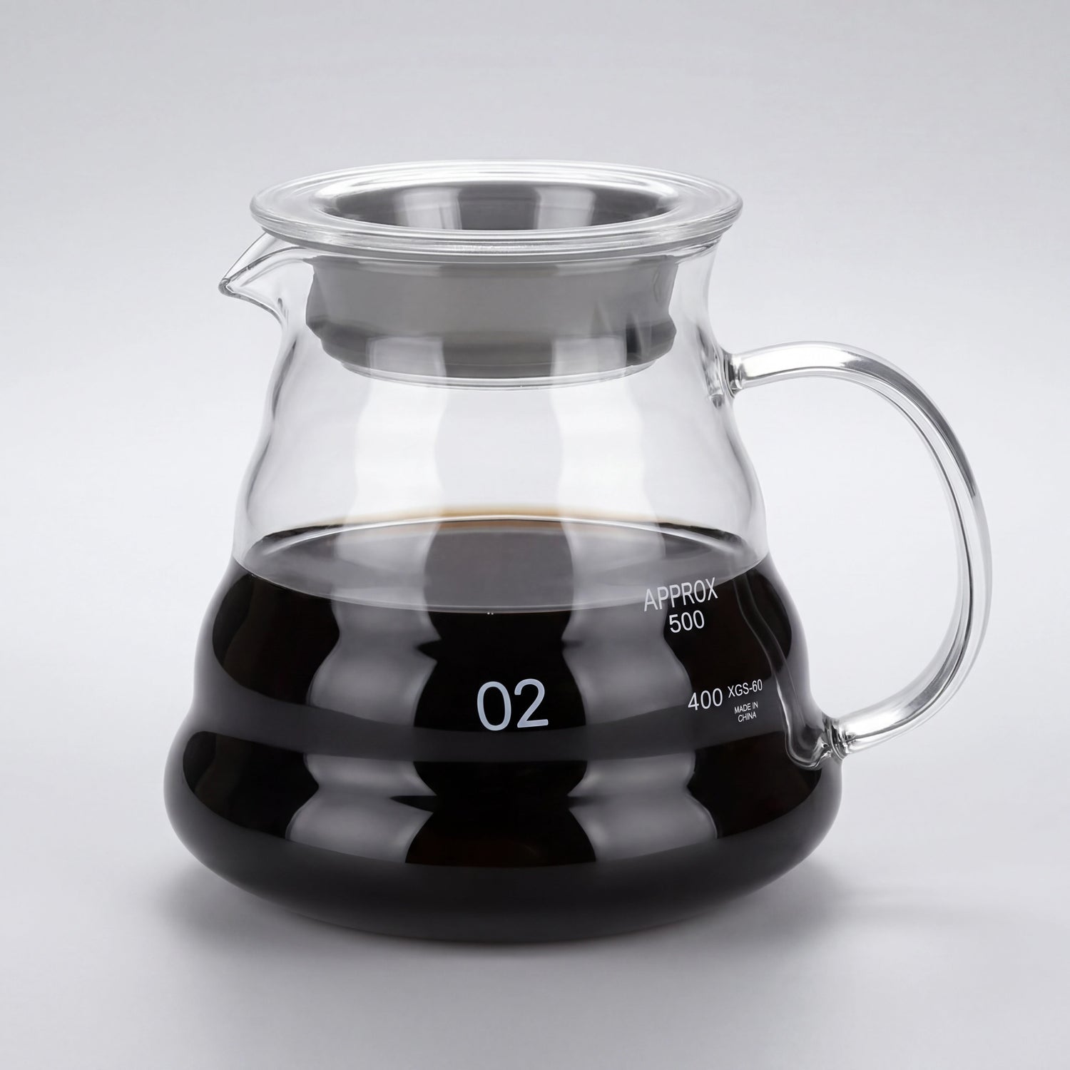 Carafe à café en verre borosilicate remplie de café, anse en verre et couvercle à liseré inox, vue de trois-quarts.