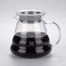 Carafe à café en verre borosilicate remplie de café, anse en verre et couvercle à liseré inox, vue de trois-quarts.