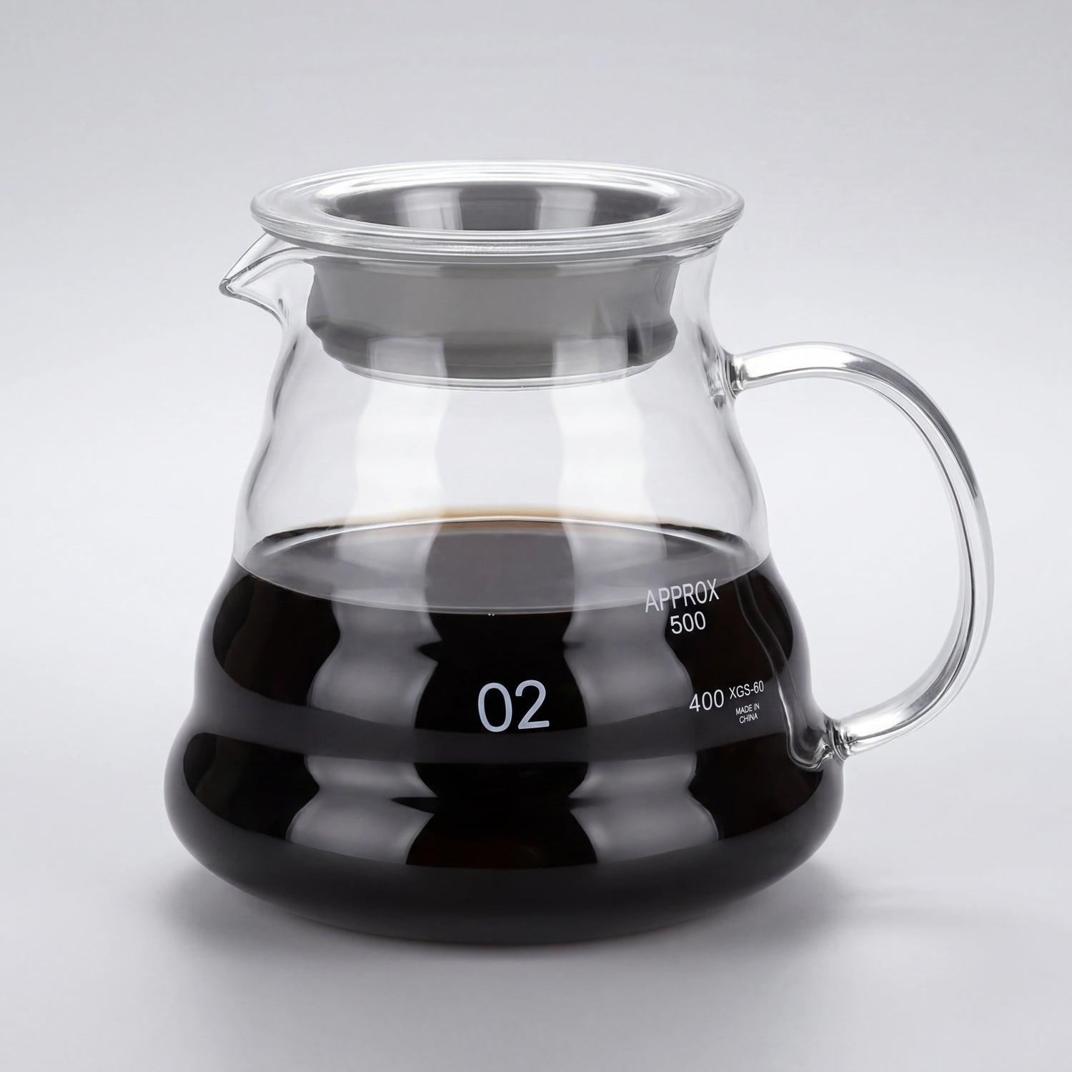 Carafe à café en verre borosilicate remplie de café, anse en verre et couvercle à liseré inox, vue de trois-quarts.