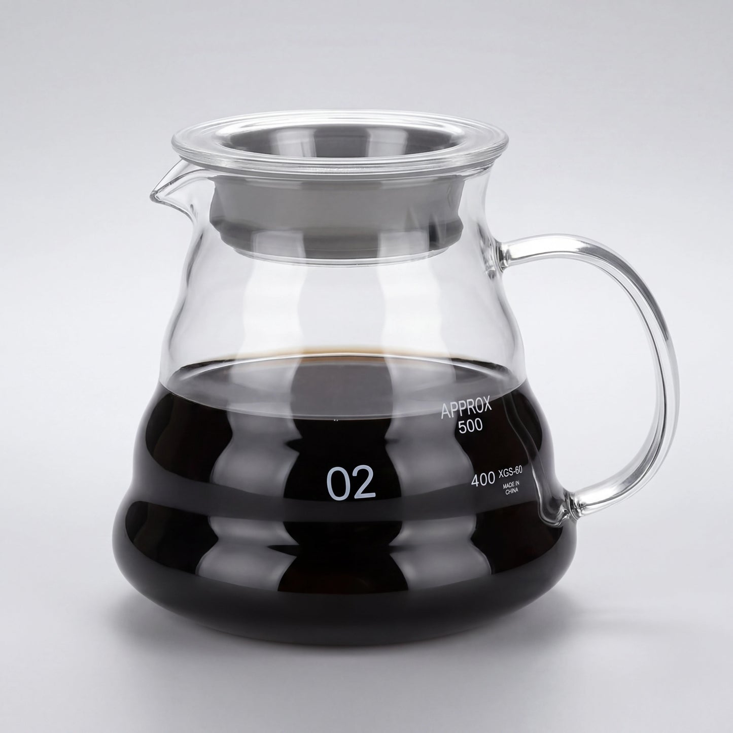 Carafe à café en verre borosilicate du kit, remplie de café, anse en verre et couvercle à liseré inox, vue de trois-quarts.