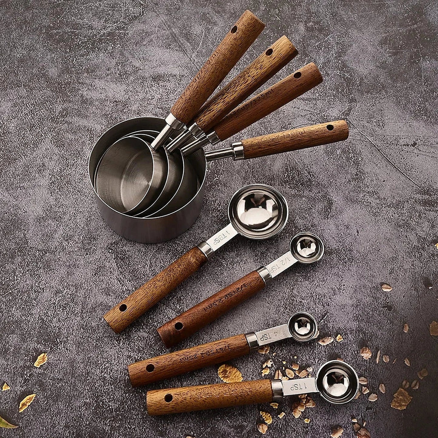 Set de tasses et cuillères doseuses en inox à manches en bois disposé sur une surface grise avec des grains de café.