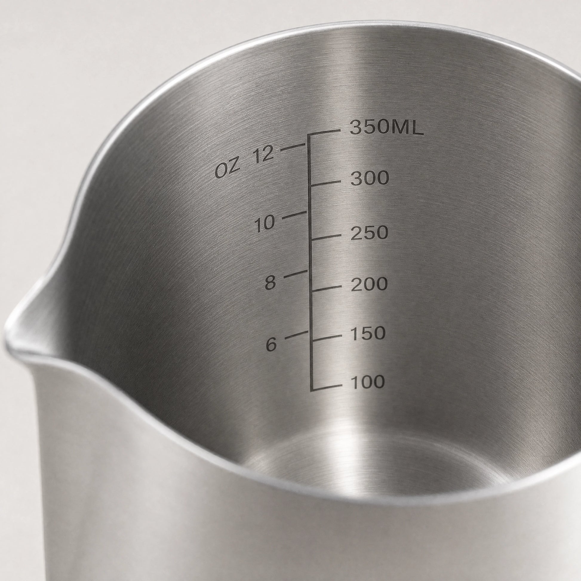 Gros plan de la graduation intérieure d'un pichet à lait en inox : repères de 100 à 350 ml et de 6 à 12 onces.