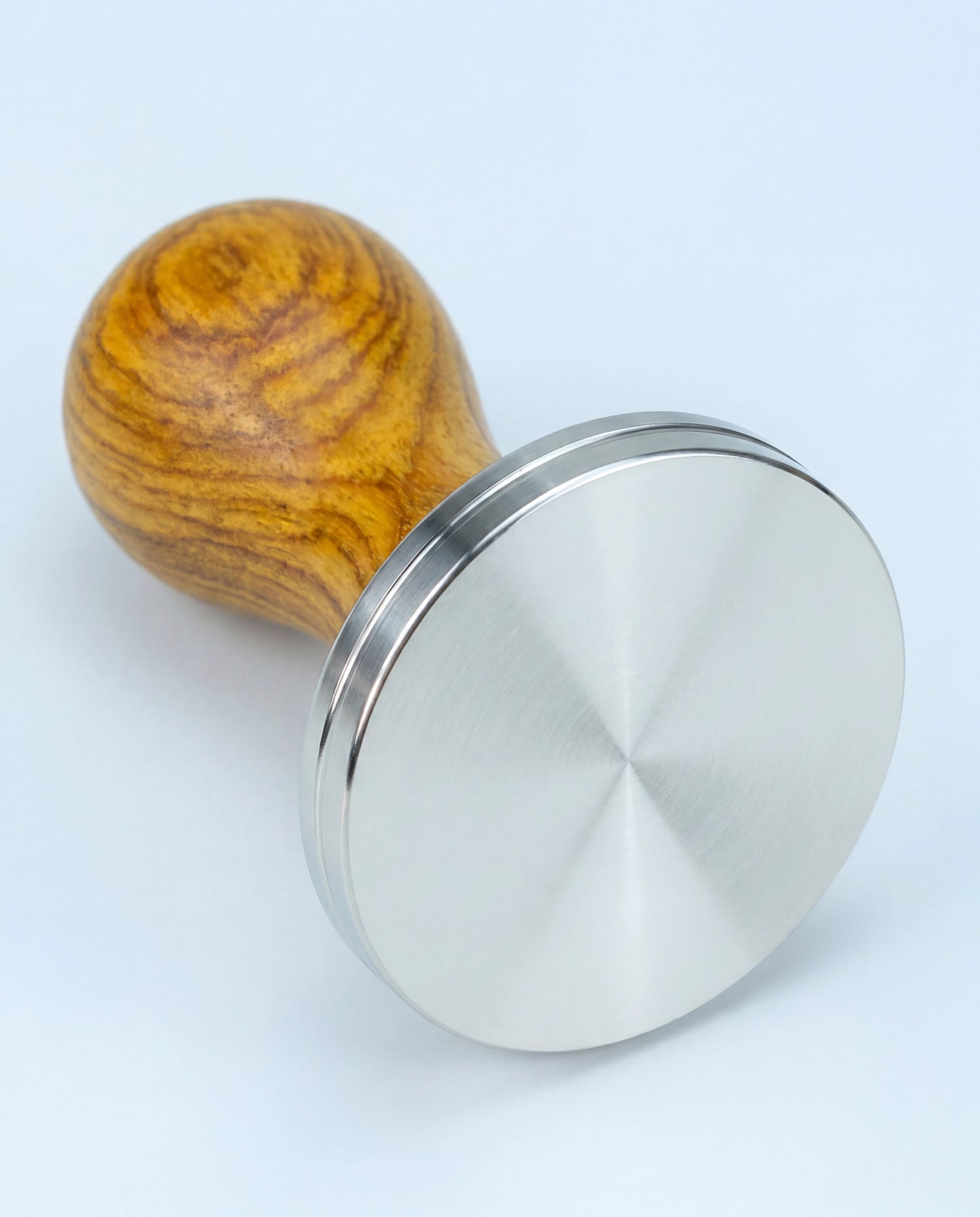 Base plate en inox d'un tamper à espresso à manche en bois, posée sur le côté.