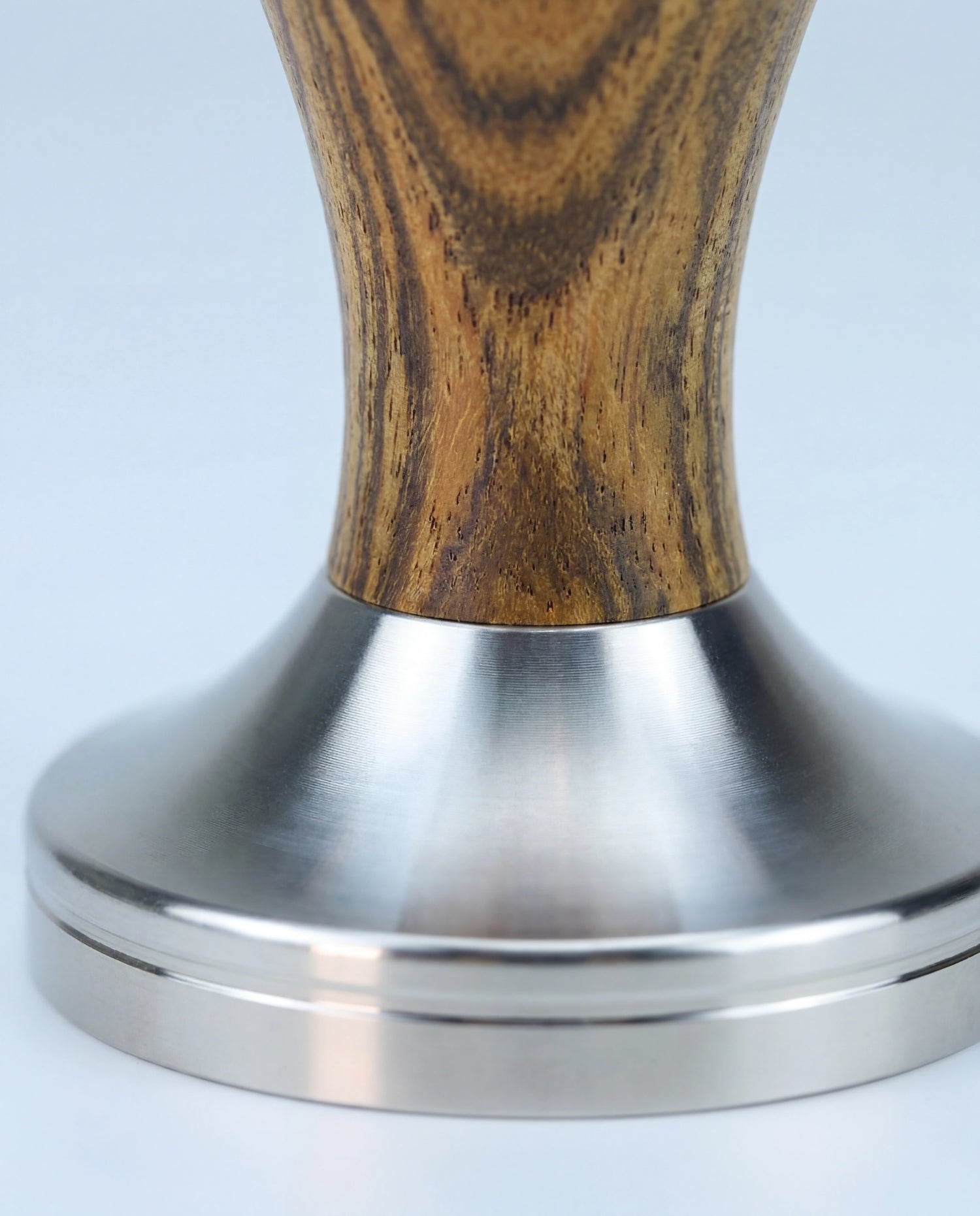 Gros plan de la jonction entre le manche en bois et la base en inox d'un tamper à espresso.