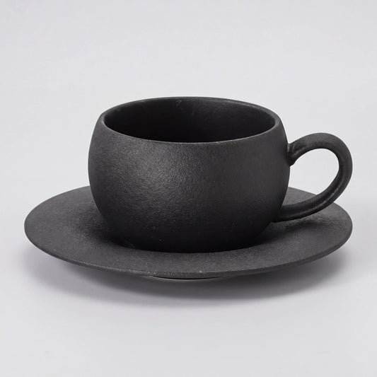 Tasse à café en céramique noire texturée avec sa soucoupe, vue de trois-quarts sur fond clair.