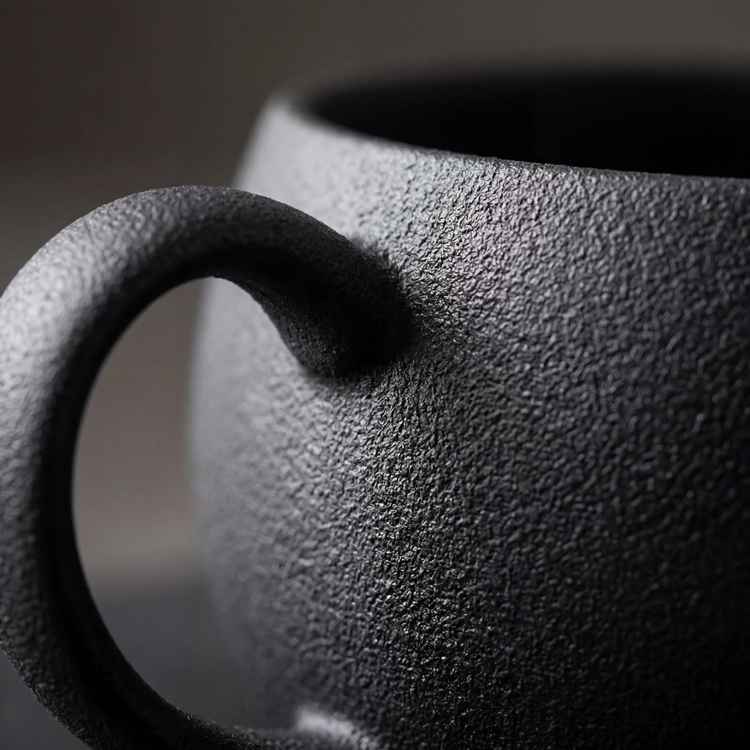 Gros plan de la texture granuleuse noire et de l'anse d'une tasse à café en céramique.