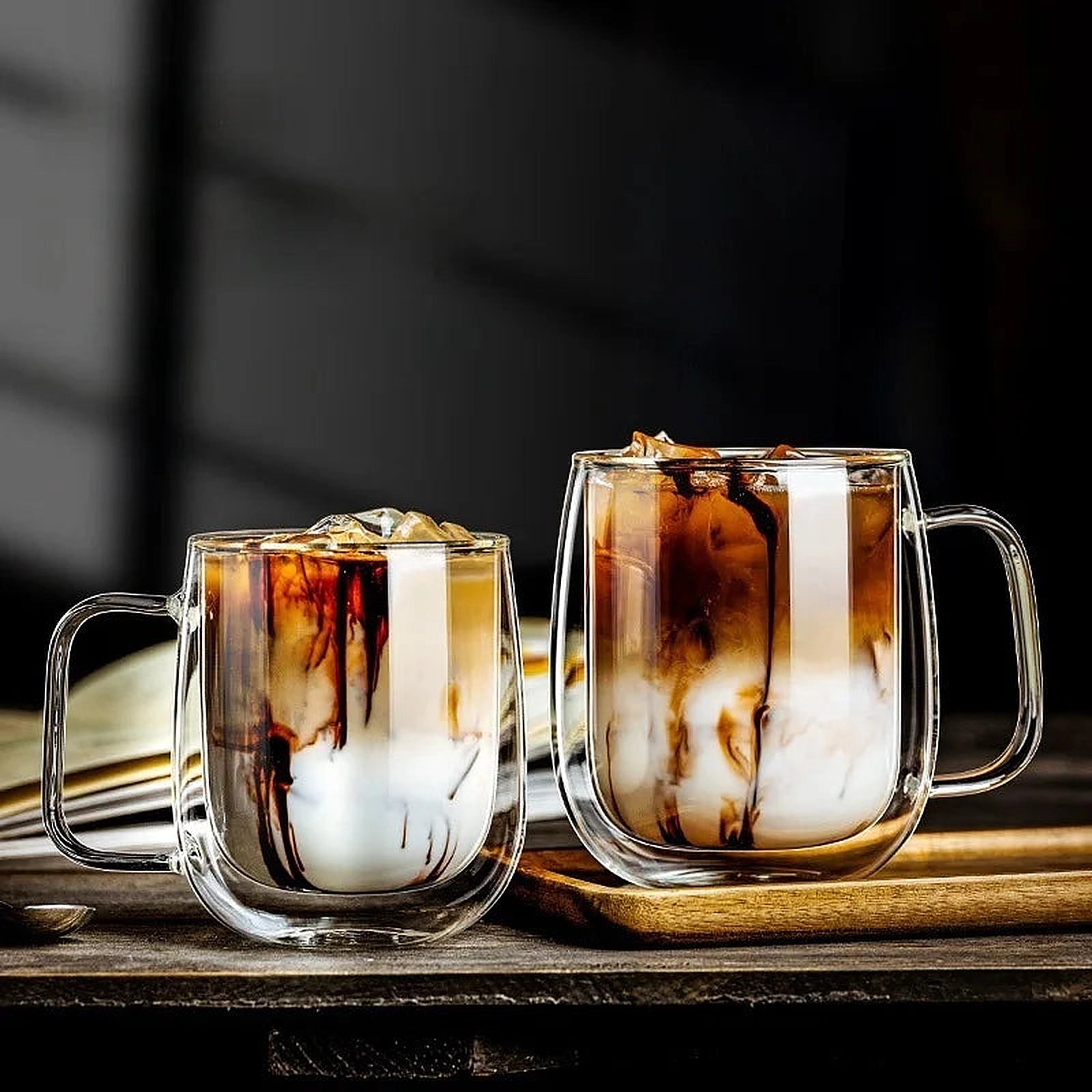 Deux verres à café double paroi avec poignée contenant des cafés glacés, sur une table en bois.