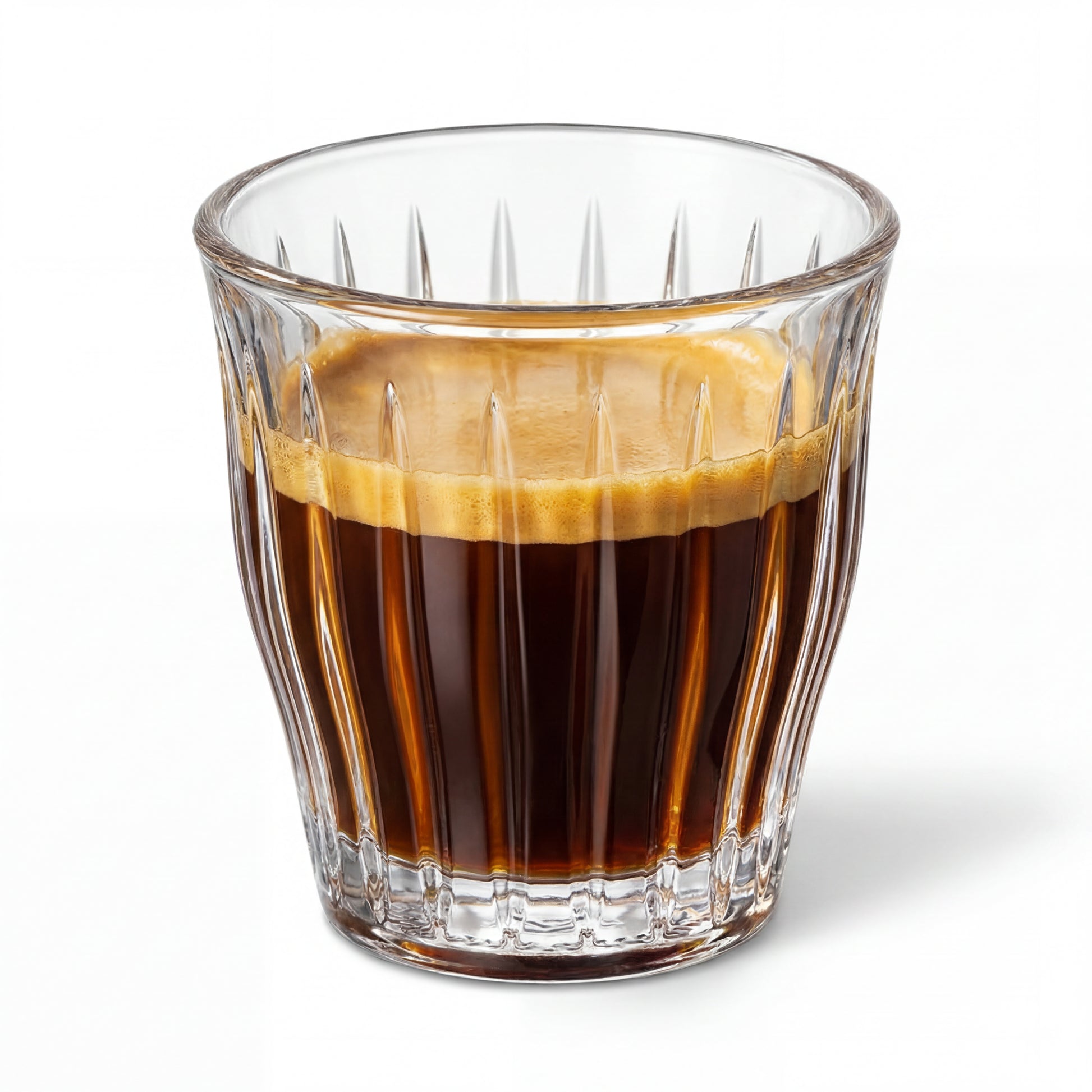 Verre à espresso facetté transparent contenant un espresso, sur fond blanc.