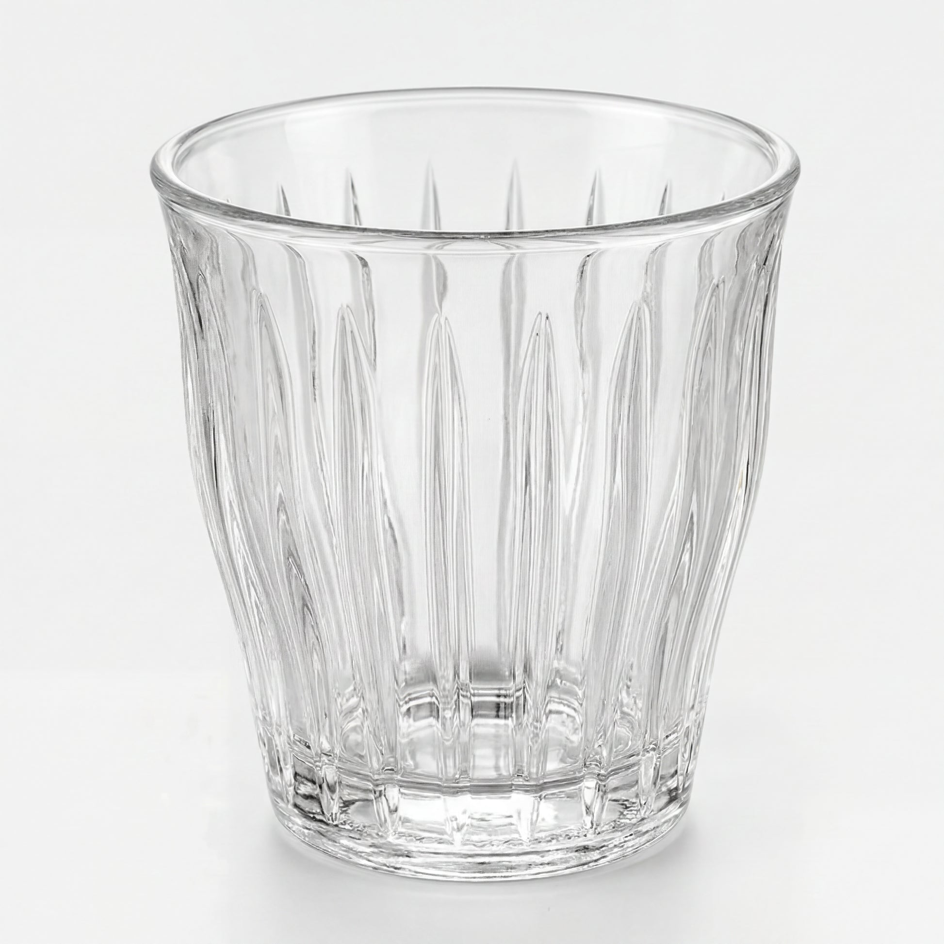 Verre à espresso transparent à facettes verticales, vue de trois-quarts sur fond blanc.